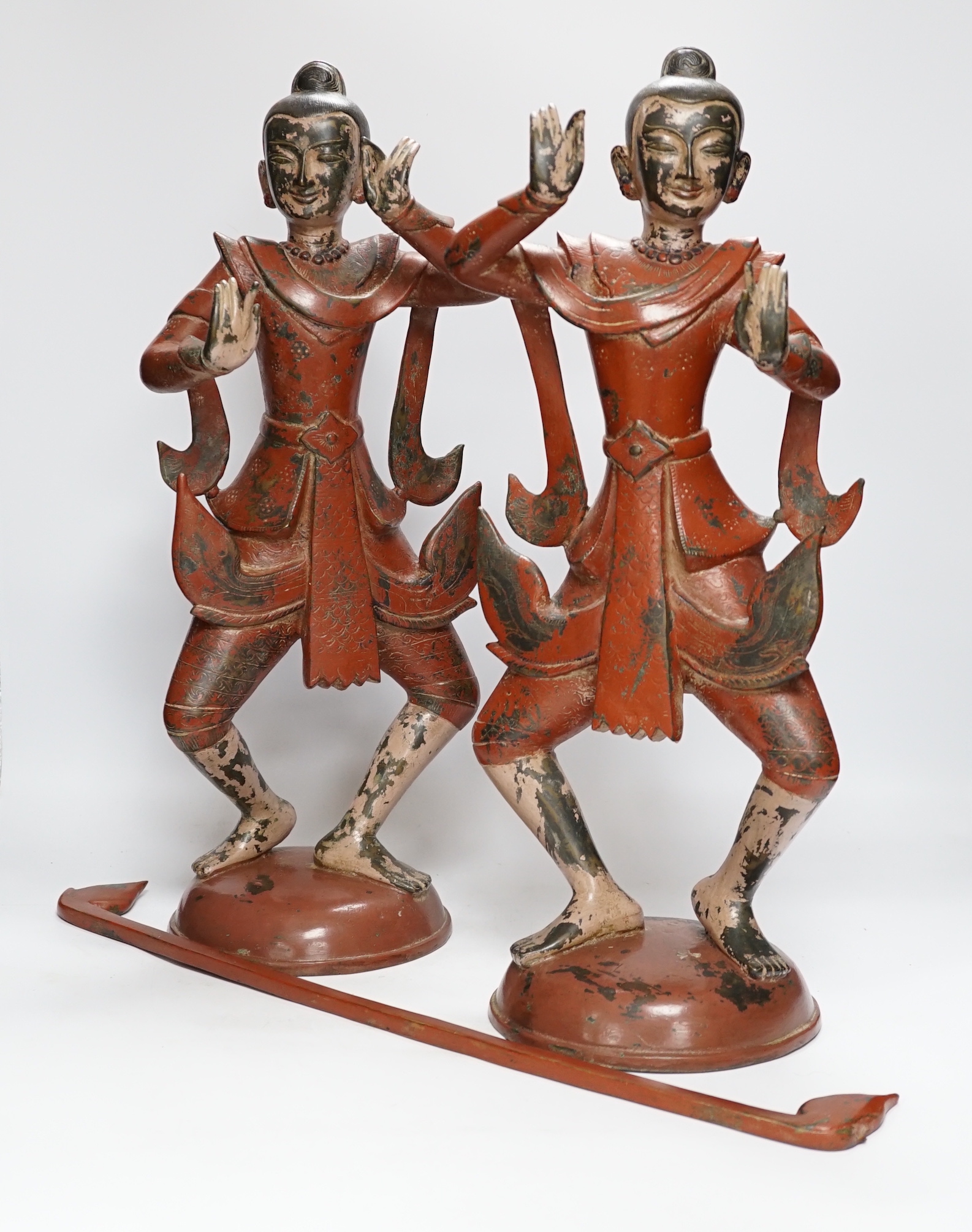 A pair of Thai red ochre painted bronze figures of traditional dancers with decorative rod on circular bases, 50cm